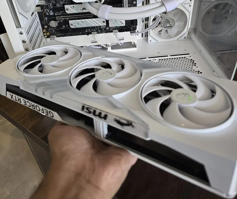 A white triple-fan graphics card held beside an open PC case at GetPC